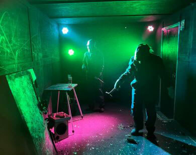 two people in a rage room with colorful lights smashing things